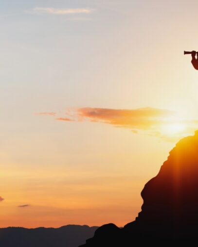 man looking through binoculars atop a mountain