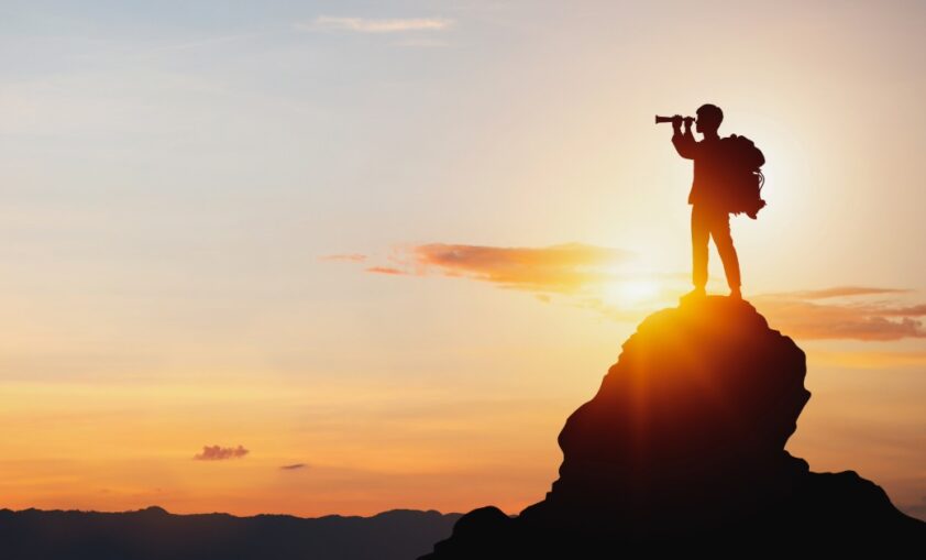 man looking through binoculars atop a mountain