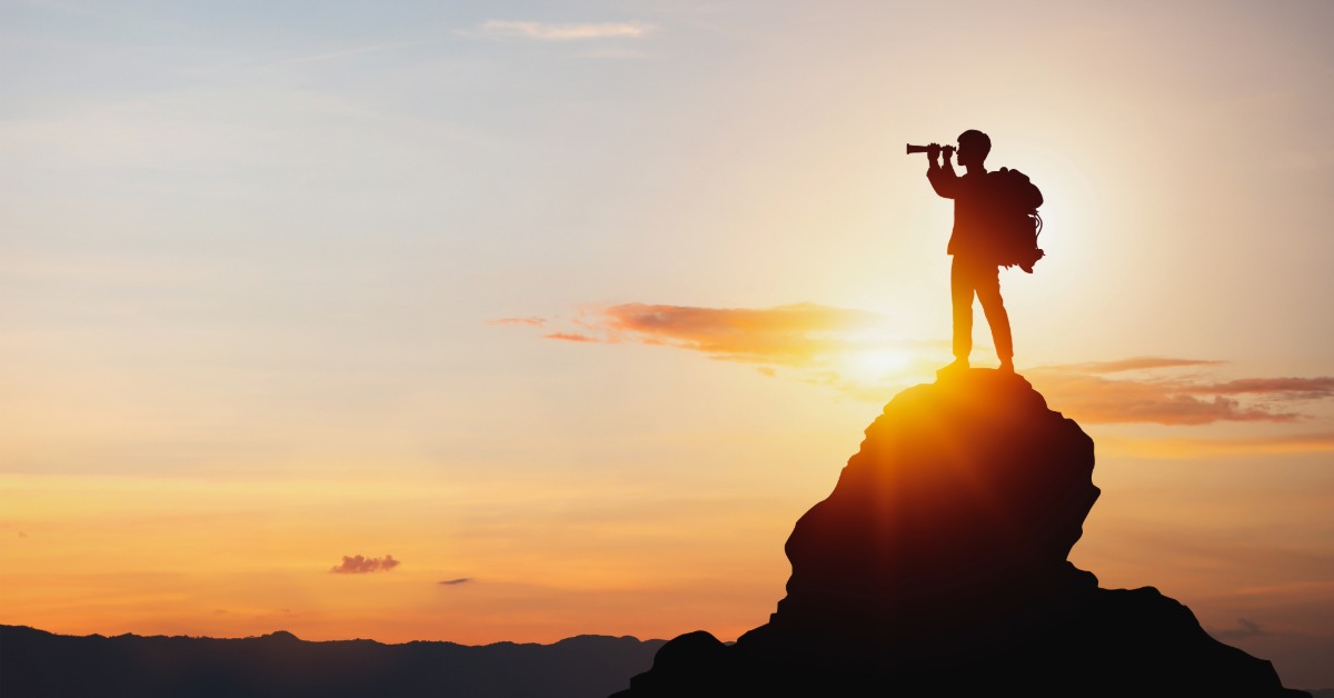man looking through binoculars atop a mountain